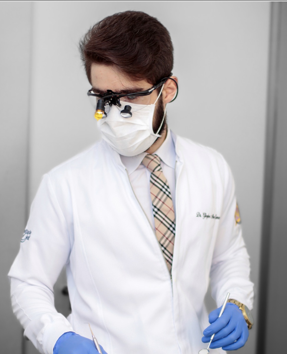 Dr. Gleyber Lemos em atendimento clínico, com lupa e instrumental